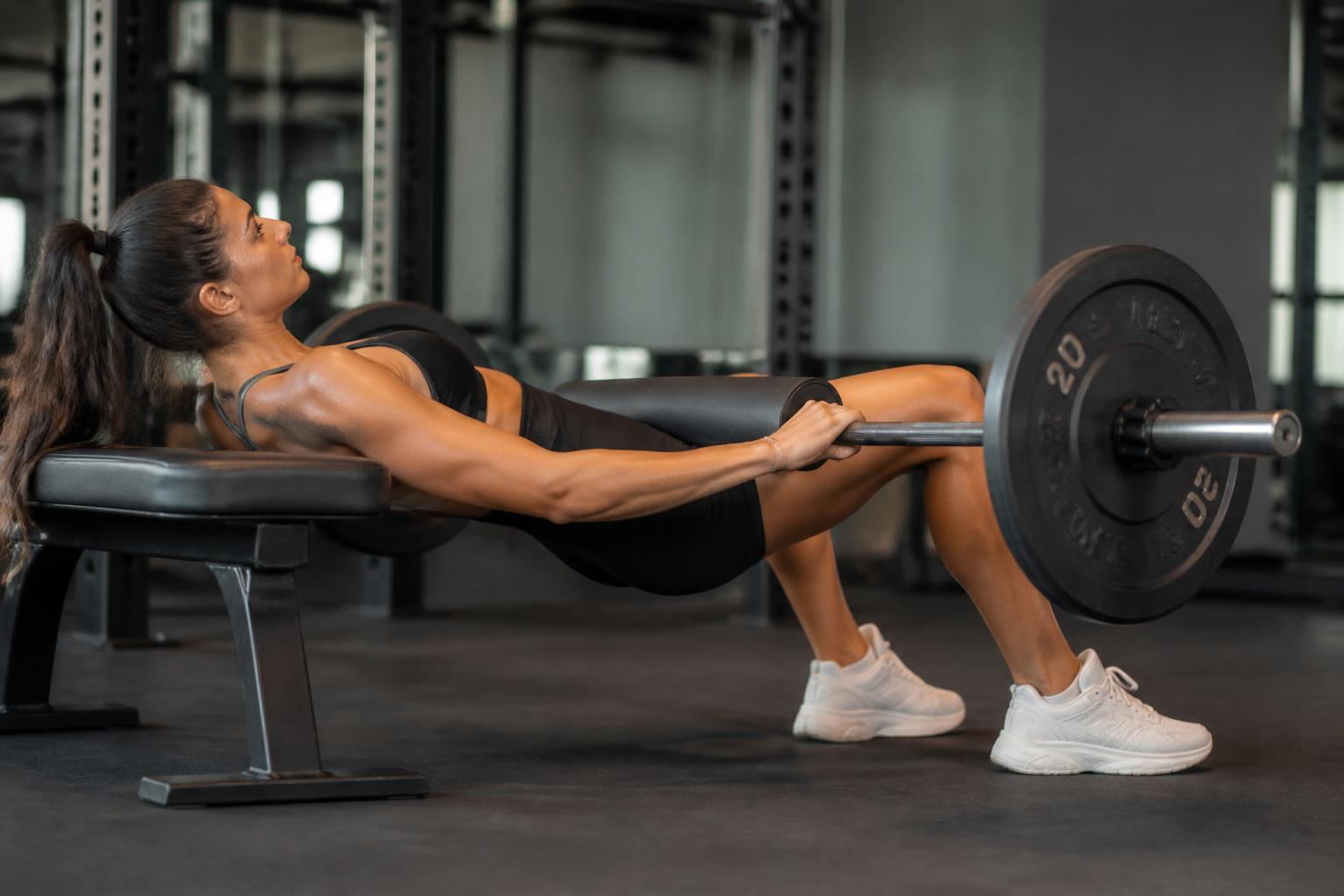 En kvinna gör hip thrust med skivstång över höfterna och övre ryggen mot en bänk